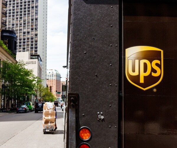 ups logo is shown on a black delivery truck with high rise buildings in the background
