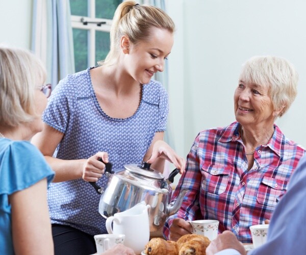 seniors socializing while a young woman pours tea