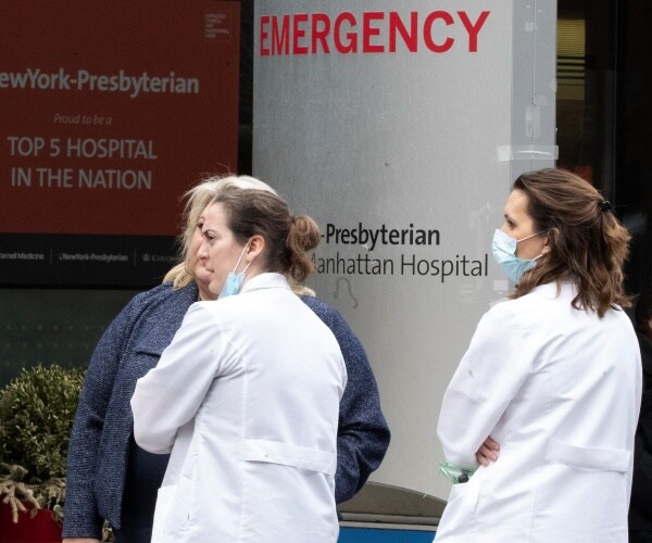 doctors in white coats and face masks stand outside emergency room of a hospital