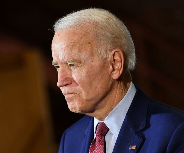 biden in a suit and burgundy tie with brown background