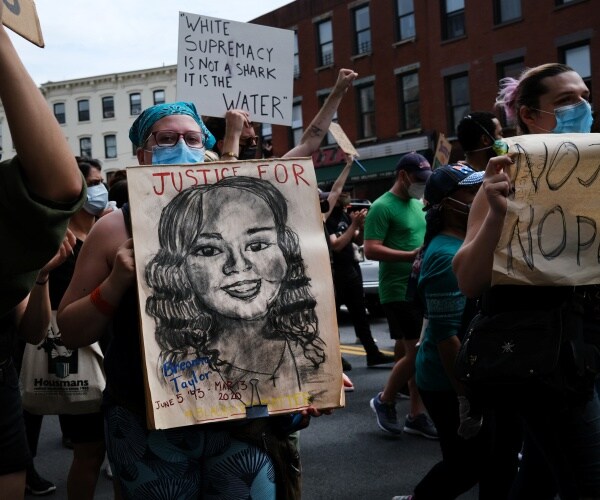 woman at a protest holds a poster with a drawing of breonna taylor