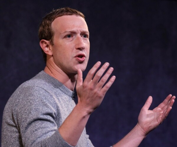 mark zuckerberg in a gray shirt speaking with his hands raised up