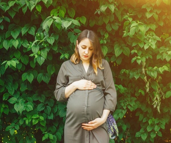 woman in a green dress holding her pregnant belly