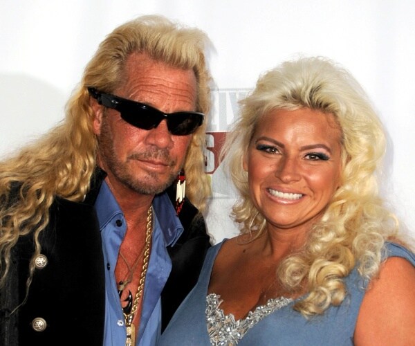 duane chapman in a blue shirt and black coat wearing sunglasses and beth wearing a blue dress