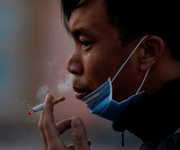 man smoking a cigarette while wearing a face mask pulled down around his chin