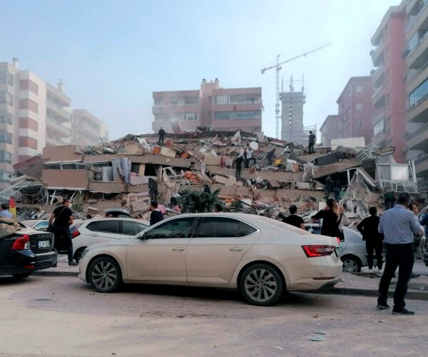 people stand in front of collapsed building