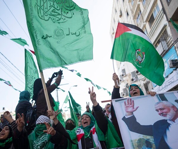 women in head coverings wave flags for hamas