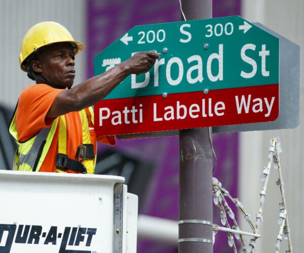 a worker in a bucket hangs a sign reading patti labelle way below a sign reading broad street