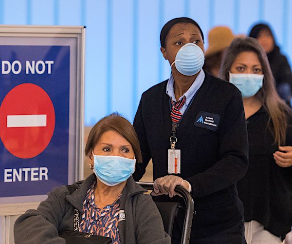 airport travelers walk through the terminal wearing masks