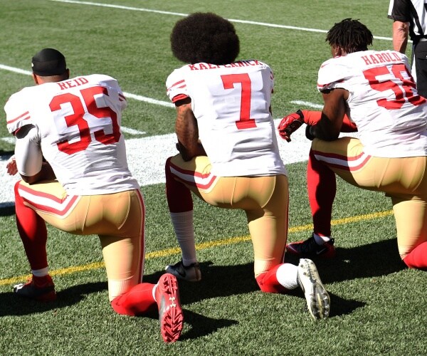football players in white red and yellow uniforms kneeling