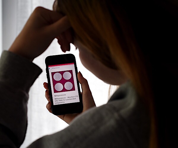 a girl rests her head in her hand as she looks at her phone to order mifepristone