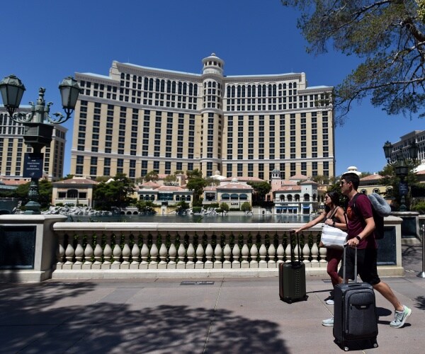 bellagio is seen facing the water with people carrying suitcases walking by