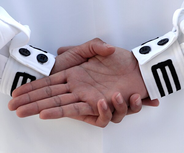 the hands of a navy sailor are interlocked behind his back