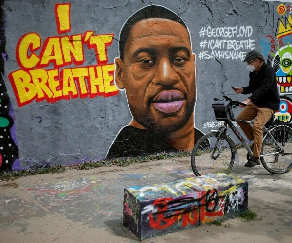 man in a mask bikes by a mural of floyd with words "I can't breathe" next to it