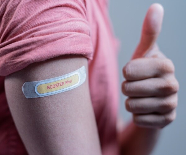 person with a bandage on arm that says "booster shot" giving thumbs up