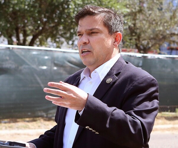 gonzalez in a suit and white dress shirt speaking to reporters outside