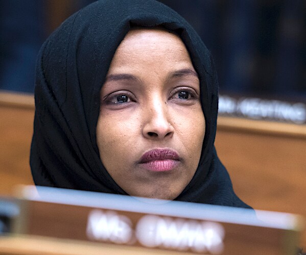 ilhan omar wears a headdress while sitting and listening during a congressional hearing