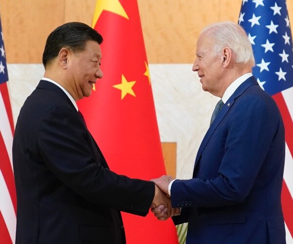 joe biden and xi jinping clasp hands over hands with us and chinese flags in background