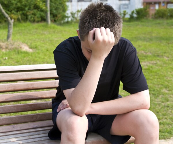a teenage boy sitting on a bench with his hand over his face