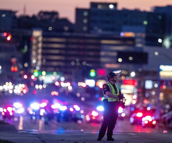 omaha police officer with gas mask standing in road with bright police car lights in the background with buildings
