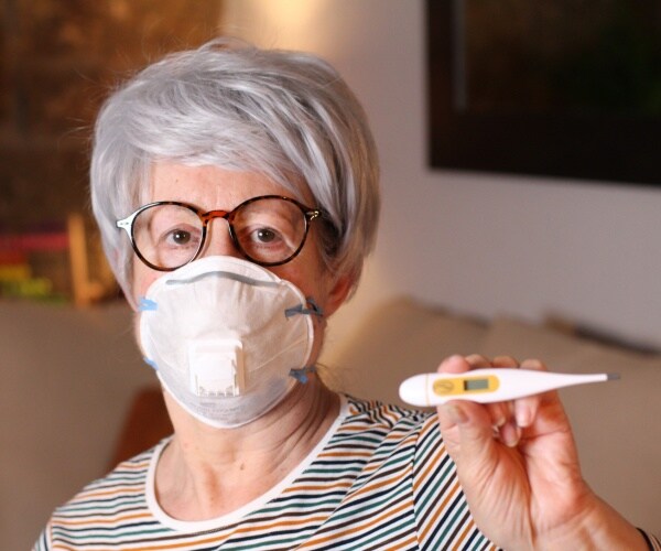 old woman with a face mask on holding up a thermometer