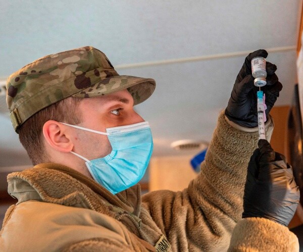 soldier wearing a blue mask and black gloves fills a syringe with the covid vaccine