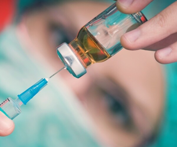 scientist with syringe in vial of vaccine