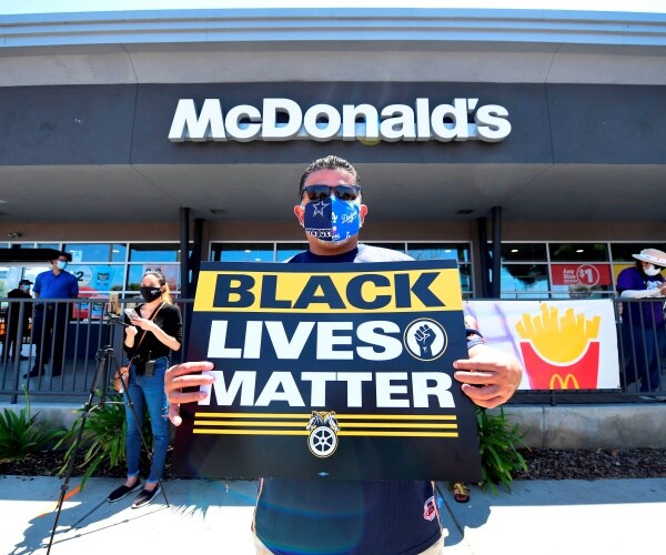 man holds up a blm sign in black and yellow in front of a mcdonald's