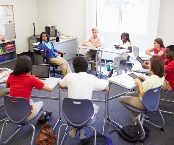 high school students in a semi-circle in desks around teacher during class