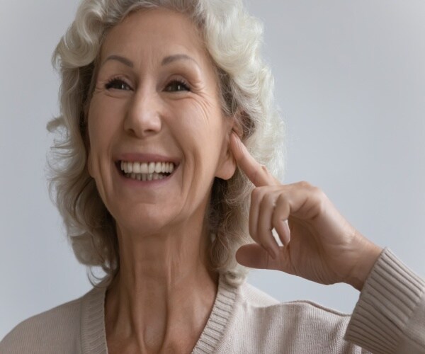 woman smiling and holding ear with a hearing device