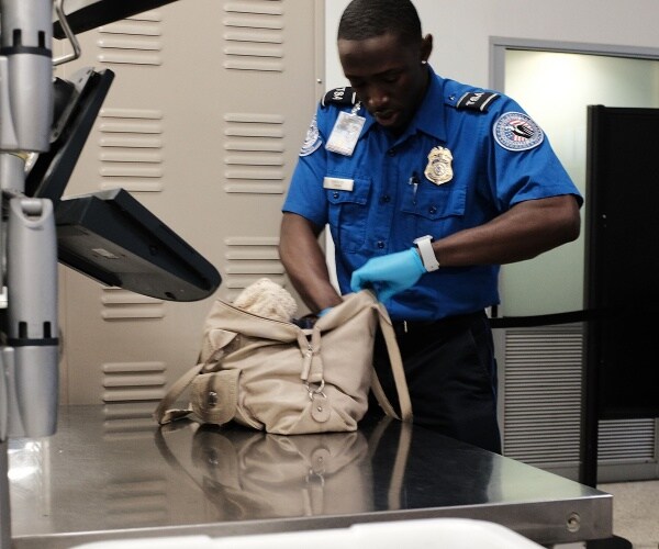 tsa worker looks through a light tan bag in the airport