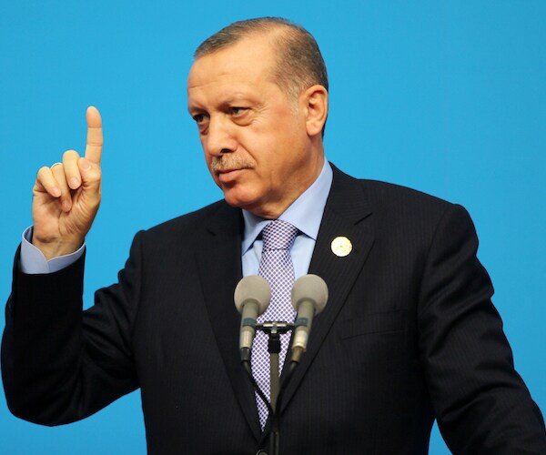 Recep Tayyip Erdoğan points his right index finger up during a news conference behind a lectern and a mic