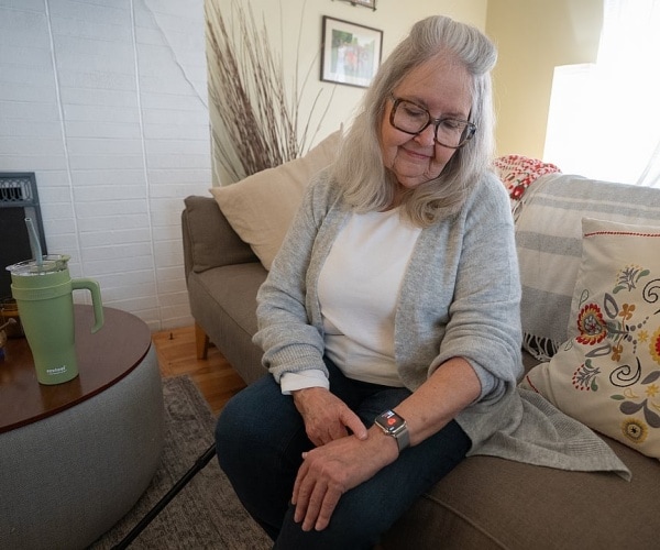older woman sitting on couch looking at smartwatch on her wrist