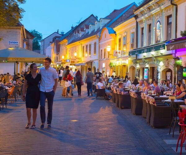 a street with busy restaurants with people walking on the street and talking and eating at the tables