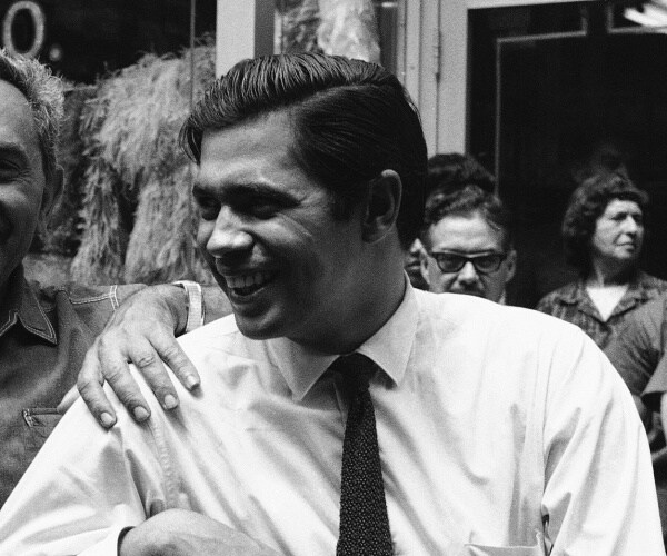 reni santoni in a light colored dress shirt and tie smiling