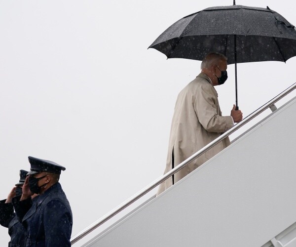 joe biden holds an umbrella and wears a mask as he walks up steps to air force one