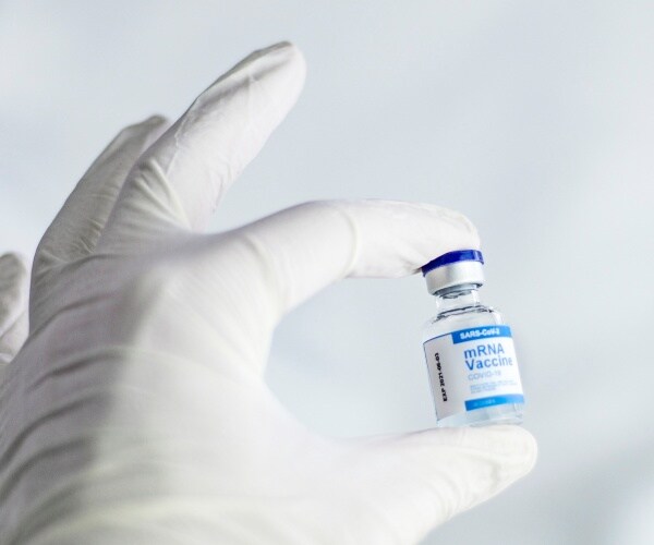 gloved hand holding vial with label 'mRNA COVID vaccine'