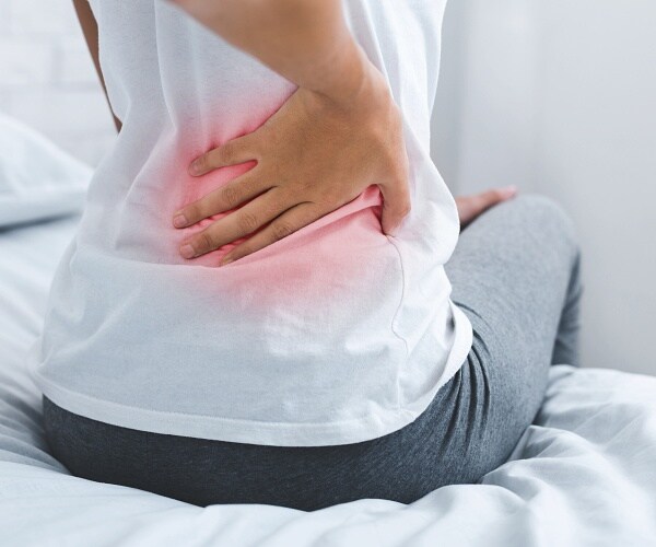 woman with lower back pain sits on bed