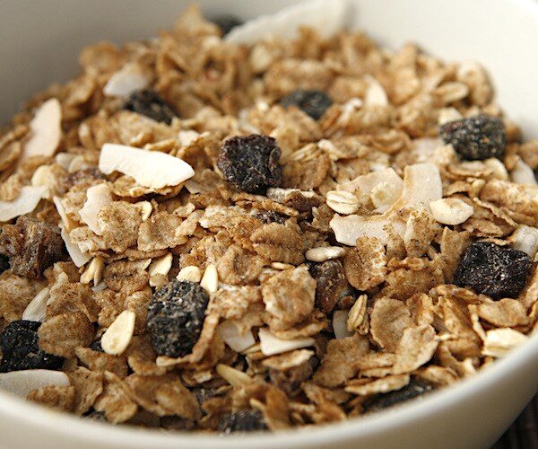 a high fiber cereal with raisins and almonds sits in a bowl with milk