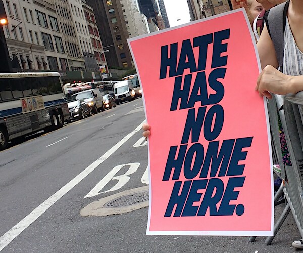 a woman holds a sign that reads hate has no home here