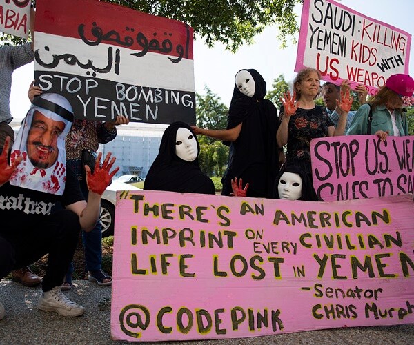 protesters with pink signs and blood on their hands protest arms sales to the saudis.