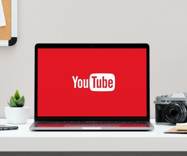 youtube logo on a laptop sitting on a desk with a plant and a camera