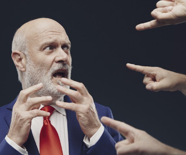 multiple hands pointing accusing fingers at man in suit and tie