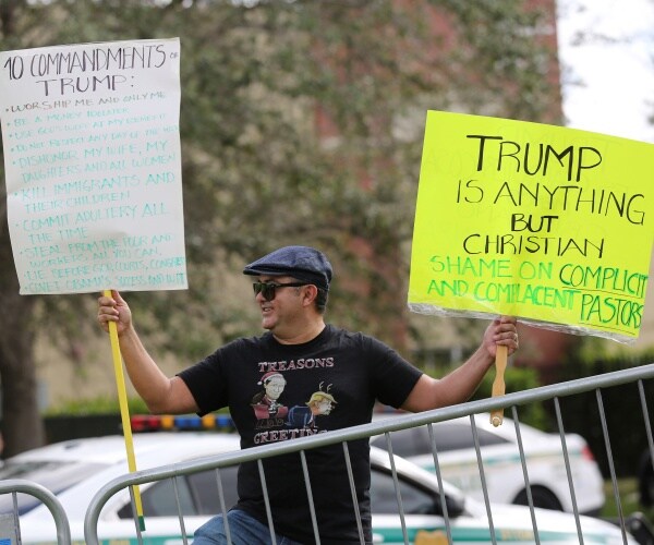 man holds up anti-trump signs outside a church