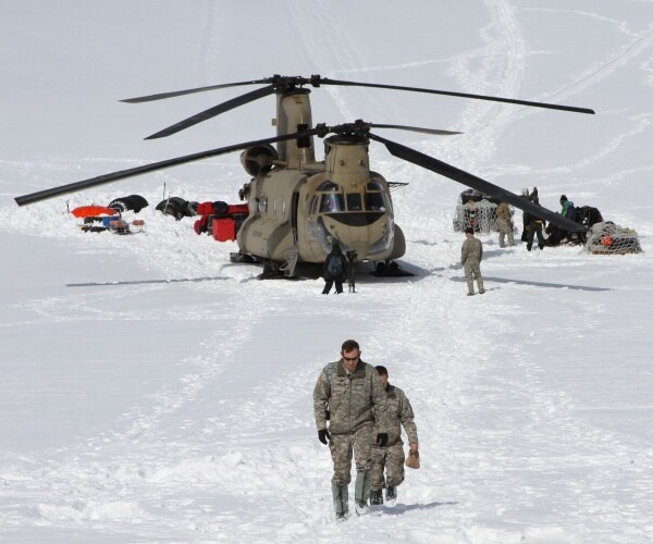 soldiers walk in front of a helicopter