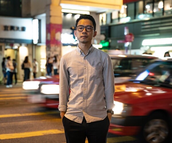 law in a light colored button down shirt and black pants standing in the road at night