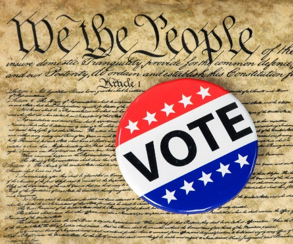 the constitution with we the people highlighted and a vote button lying on top of it